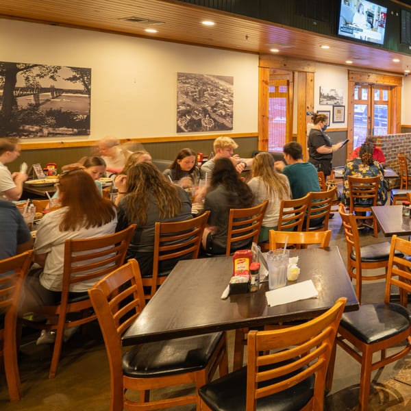 Diners seated at tables in Rusty's Riverfront Grill, with a server taking an order.