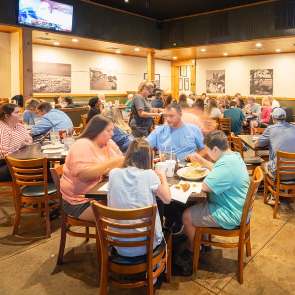 Diners enjoying meals at tables in a busy Rusty's Riverfront Grill, with a TV screen showing sports.