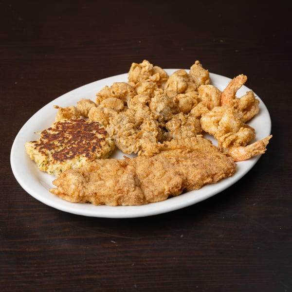 A white plate filled with golden-brown fried shrimp, oysters, fish, and a crab cake.