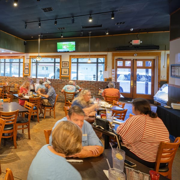 Diners seated at tables in Rusty's Riverfront Grill, with brick walls and large windows.