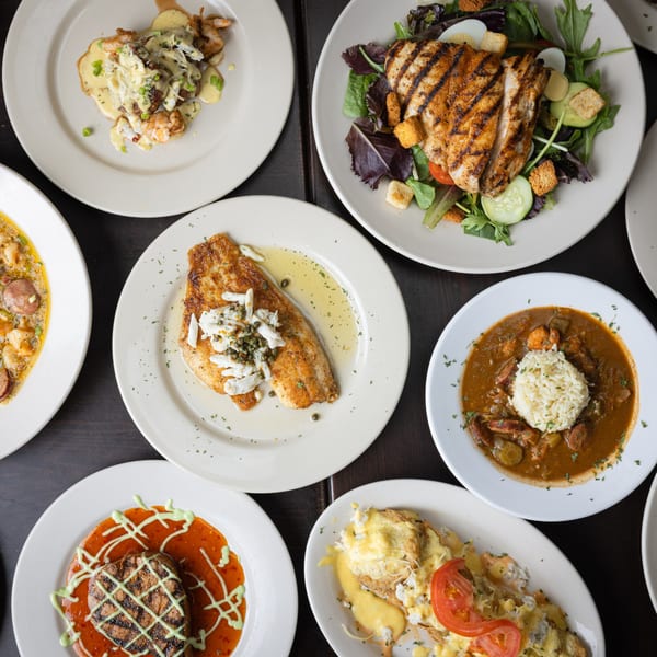 An overhead view of various seafood dishes, including grilled fish, gumbo, and shrimp and grits.