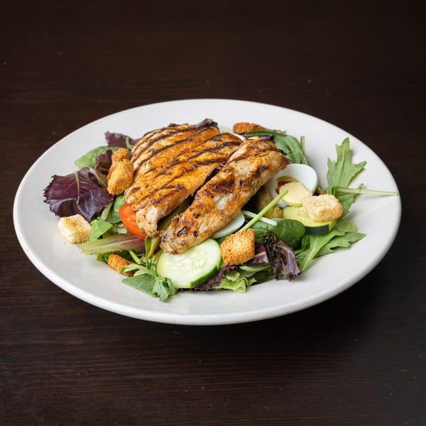 Grilled fish fillets on a bed of mixed greens with cucumber, tomato, and croutons.