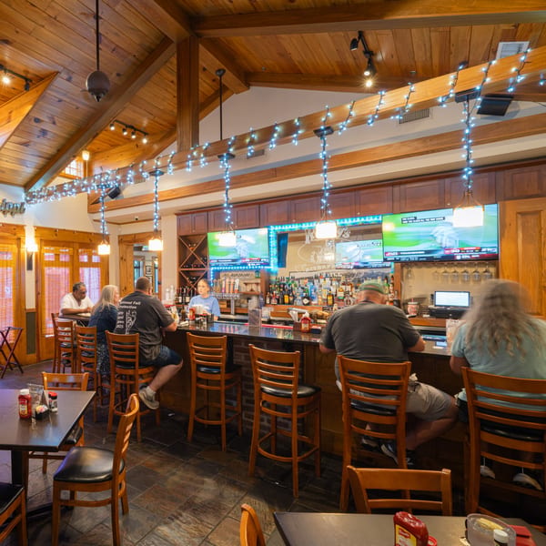 Patrons seated at the bar of Rusty's Riverfront Grill, with TVs showing sports and string lights overhead.