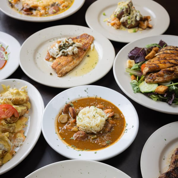 A variety of seafood dishes, including grilled fish, gumbo, and shrimp, on a dark table.