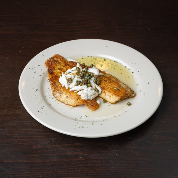 Pan-seared fish fillet topped with crab meat and capers, drizzled with a light sauce on a white plate.
